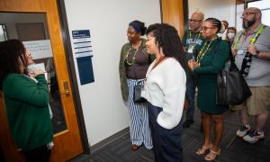 Diverse group of adults listening intently to a woman speaking in a hallway.