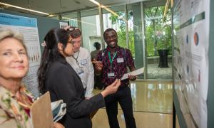 Three attendees discussing a research poster, one man smiles and points excitedly.