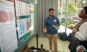 Man in blue polo explains a scientific poster to a woman at a conference.