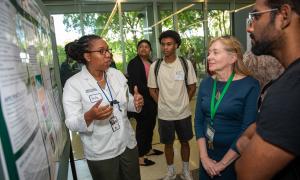 Woman in lab coat presents a scientific poster to four attentive people.