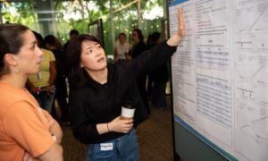 Woman in black points to a research poster, another woman in orange listens intently.