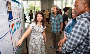 Presenter points to a scientific poster, explaining details to two attendees.