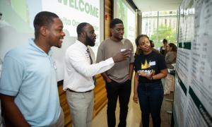 Four students discuss a research poster at an academic presentation.