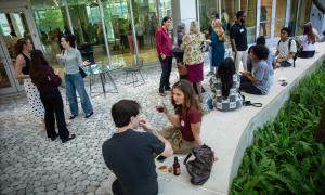 People gathered outdoors on a patio, some standing and talking, others sitting and drinking.
