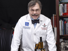 Peter Hotez, leaning on desk with old microscope in front of him