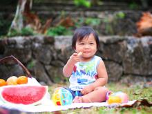 Baby Asian girl eating watermelon on a picnic blanket. 