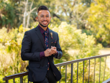 P{hD  student MIguel Lopez, wearing a suit, smiling, in a park, greenery behind him