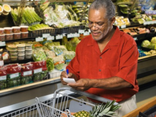 Older Black man checking a shopping list in a grocery store produce aisle.