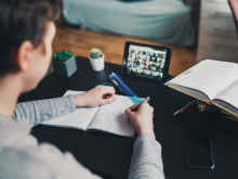Looking over the shoulder of a student taking an online course, video screen up, notebook open.