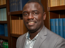 Samuel Kakraba in a grey suit jacket in front of bookshelves