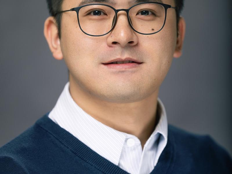 Man with glasses smiling, wearing a navy blue sweater and white shirt.