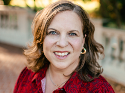 Dr. Katherine MIlls, smiling, with brown hair and blue eyes in a red patterned shirt.