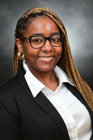 Smiling woman with glasses and golden braids in a black blazer.