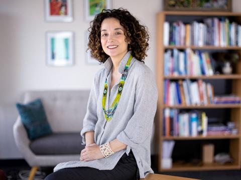 Alessandra Bazzano, sitting on a desk, smiling for camera, in her office