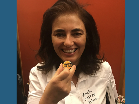 Arachu Castro, smiling, holding a small button that reads "Health FOr All," from the 2020 UN meeting