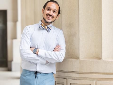 Kristefer Stojanovski standing, arms crossed, in front of a column, wearing a bow tie, smiling